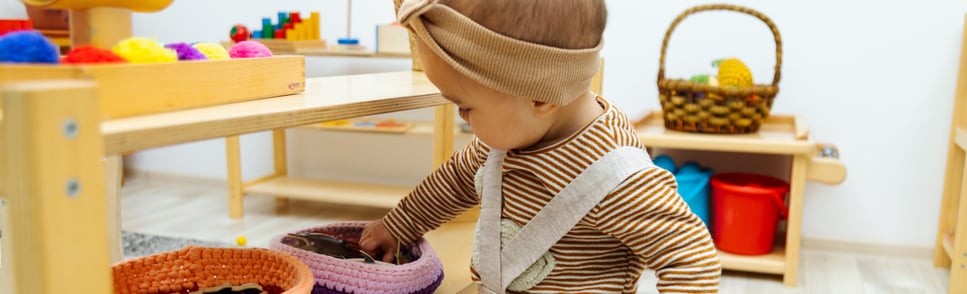 A young child exploring a Montessori-style playroom with organized baskets and shelves, demonstrating child-led learning and independence.
