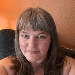 A photo of a smiling woman with highlighted hair, bangs and blue eyes.
