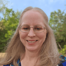 A picture of a smiling woman with strawberry blonde hair and glasses
