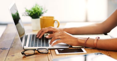 Woman typing on a laptop at a wooden desk, researching options before hiring a personal assistant