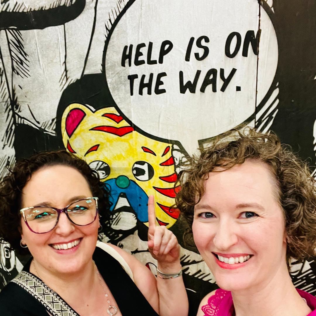Kate Ginsberg and Heather Snaman pose with a sign that says Help is On The Way symbolizing the services and support offered by Queen of To Do Kate Ginsberg and Heather Snaman pose with a sign that says Help is On The Way symbolizing the services and support offered by Queen of To Do