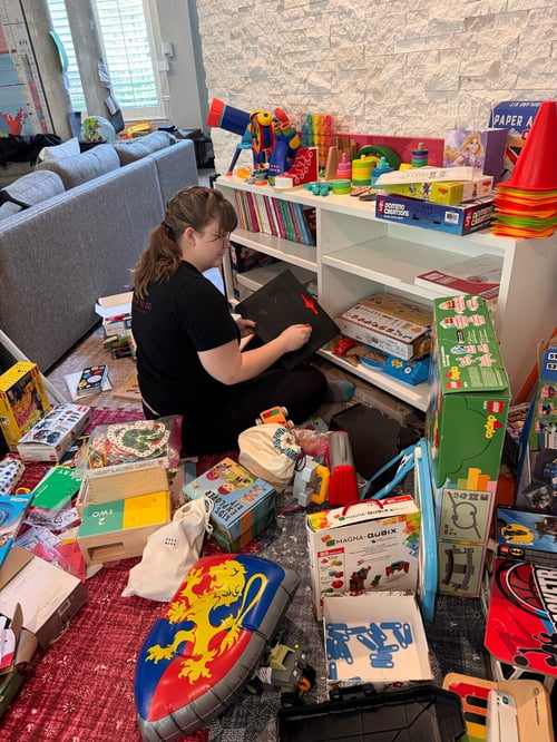 Queen of To Do team member Shianne organizing childrens toys, books, and games on a bookshelf