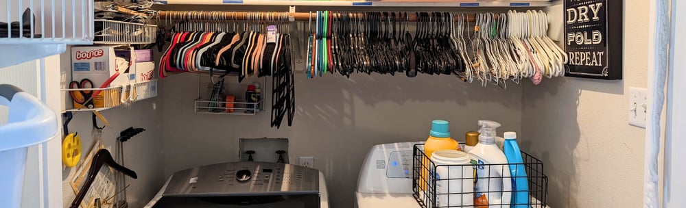 Tidy laundry room with neatly arranged hangers and laundry supplies above washer and dryer.